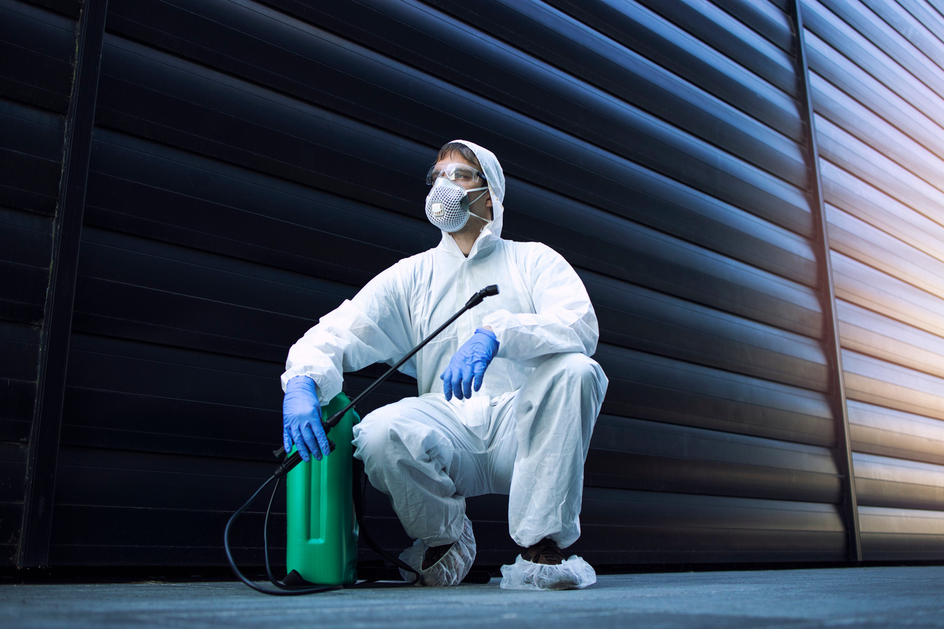 Pest control. Man in white protective suit by sprayer reservoir tank with poison and chemicals to stop spreading insects and rodents.